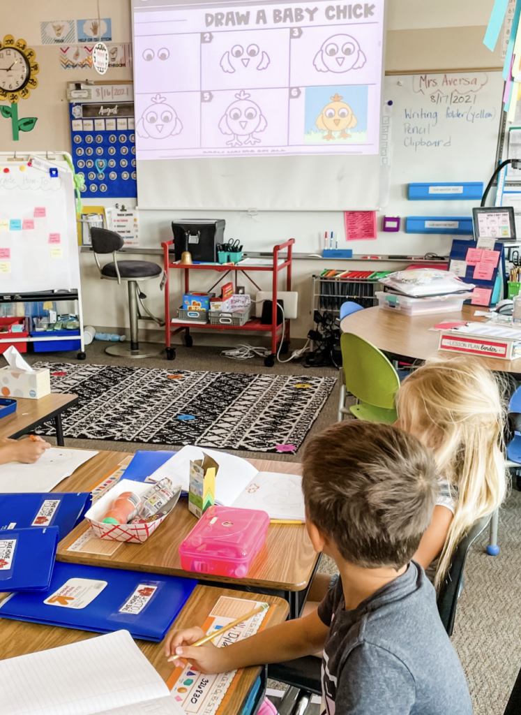 Students watching a “Draw a Baby Chick” tutorial projected on a classroom screen during a digital drawing activity.